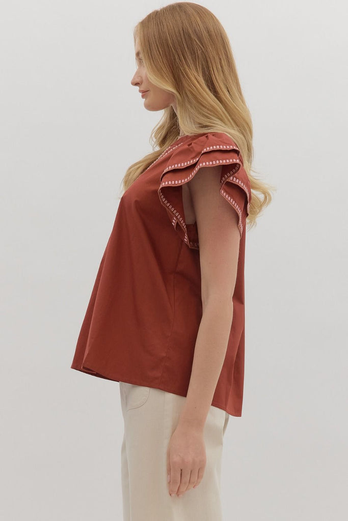 A solid brick-red top with tiered ruffle flutter sleeves. The v-neckline and sleeve ruffles have a white contrast embroidered stitching.