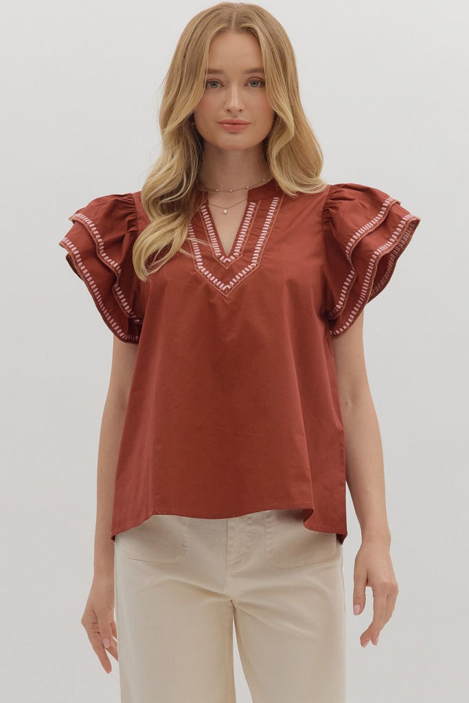 A solid brick-red top with tiered ruffle flutter sleeves. The v-neckline and sleeve ruffles have a white contrast embroidered stitching.