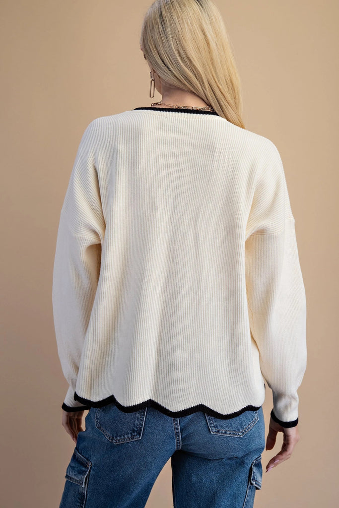 An ivory knit sweater featuring a black contrasting trim on the crew neckline and a distinctive wavy black hem.