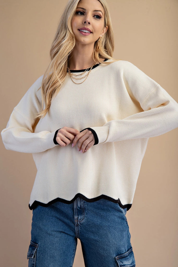 An ivory knit sweater featuring a black contrasting trim on the crew neckline and a distinctive wavy black hem.
