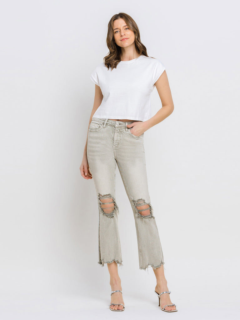 Woman wearing a white t-shirt and light moss green jeans with ripped knees on a white background