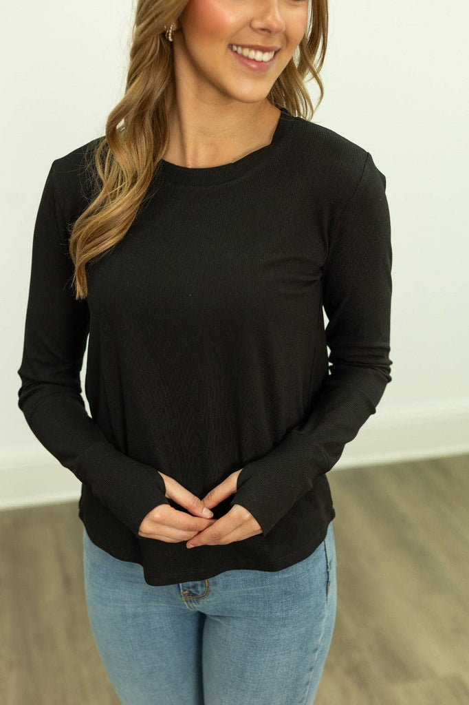 Woman wearing a black ribbed long sleeve top paired with jeans.