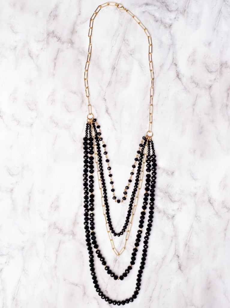 Layered black crystal and gold paperclip chain necklace with multiple strands.