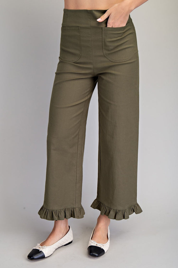 Close-up of a woman wearing high-rise olive green straight leg pants with oversized patch pockets and ruffled hems, styled with cream and black ballet flats.