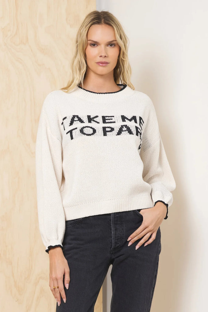 An ivory jacquard knit sweater with the phrase "Take Me To Paris" in black lettering on the front. It has a crew neck with black trim and long, balloon-style sleeves.