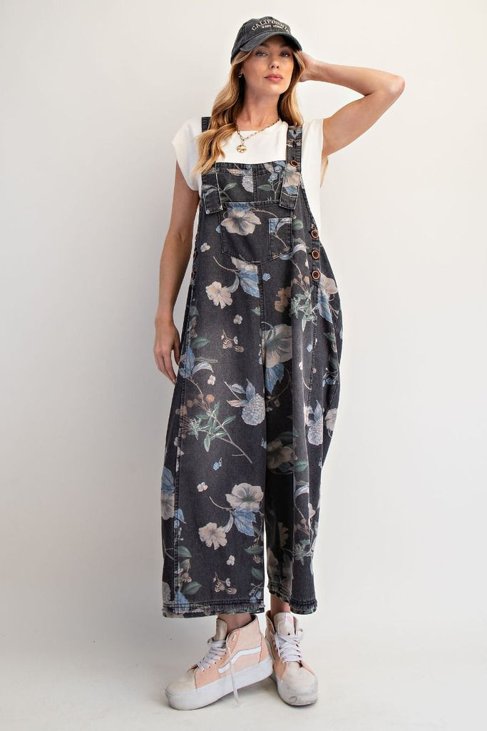 Fun, casual washed black denim overalls with an allover floral print, cropped legs, adjustable shoulder straps, bib pocket, side button closures, and oversized back patch pockets.