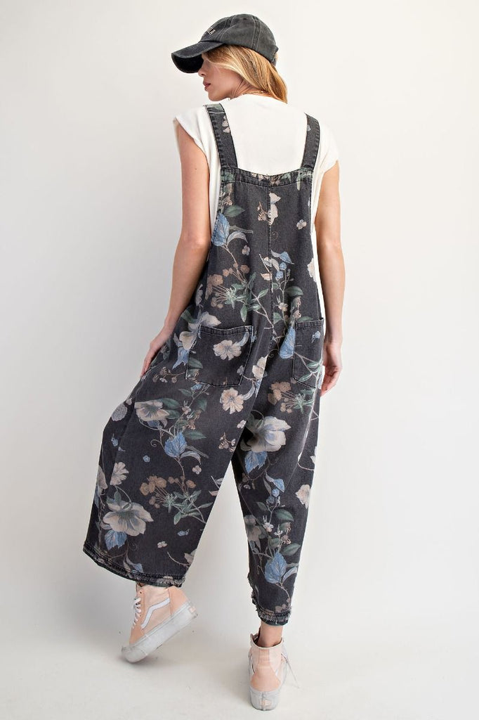 Fun, casual washed black denim overalls with an allover floral print, cropped legs, adjustable shoulder straps, bib pocket, side button closures, and oversized back patch pockets.
