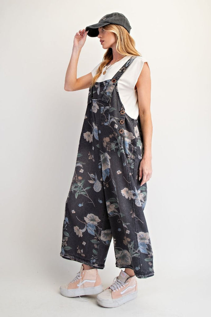 Fun, casual washed black denim overalls with an allover floral print, cropped legs, adjustable shoulder straps, bib pocket, side button closures, and oversized back patch pockets.
