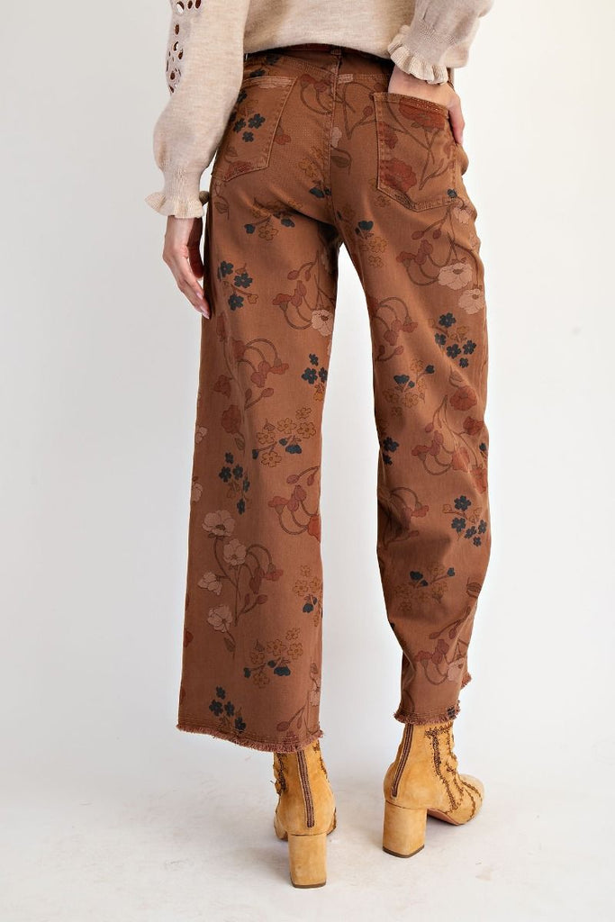 A pair of mocha-colored, high-waisted, wide-leg pants with a warm-toned floral print. The pants are cropped with a frayed hem.