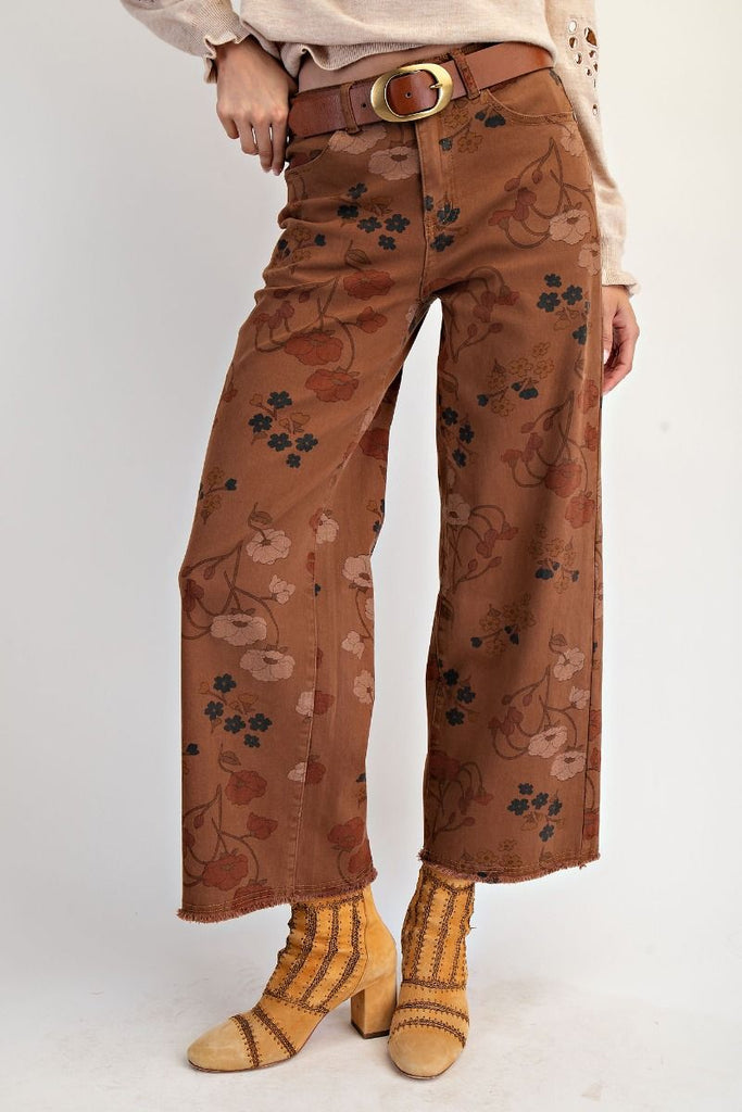 A pair of mocha-colored, high-waisted, wide-leg pants with a warm-toned floral print. The pants are cropped with a frayed hem.