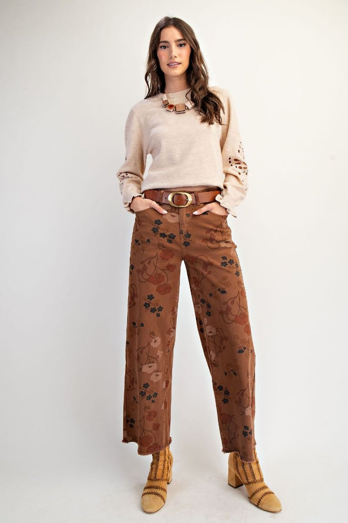 A pair of mocha-colored, high-waisted, wide-leg pants with a warm-toned floral print. The pants are cropped with a frayed hem.