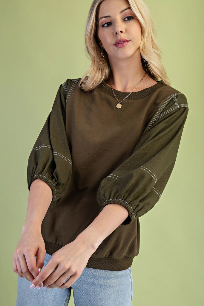 Olive mixed-fabric top with ¾ length sleeves, contrast stitching, crew neckline, and relaxed fit