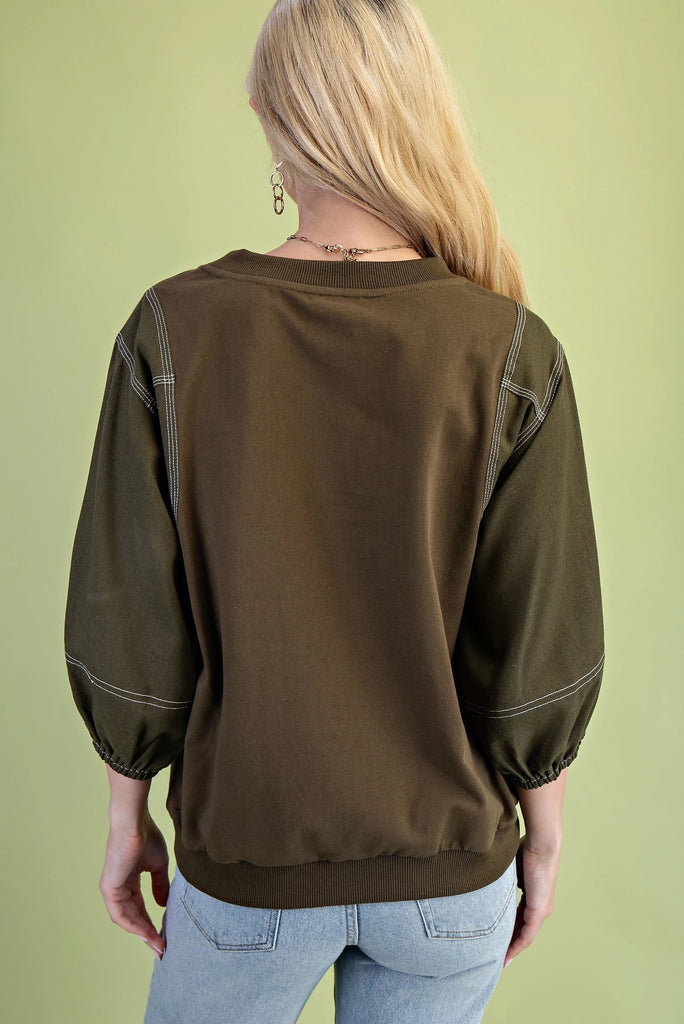 Olive mixed-fabric top with ¾ length sleeves, contrast stitching, crew neckline, and relaxed fit
