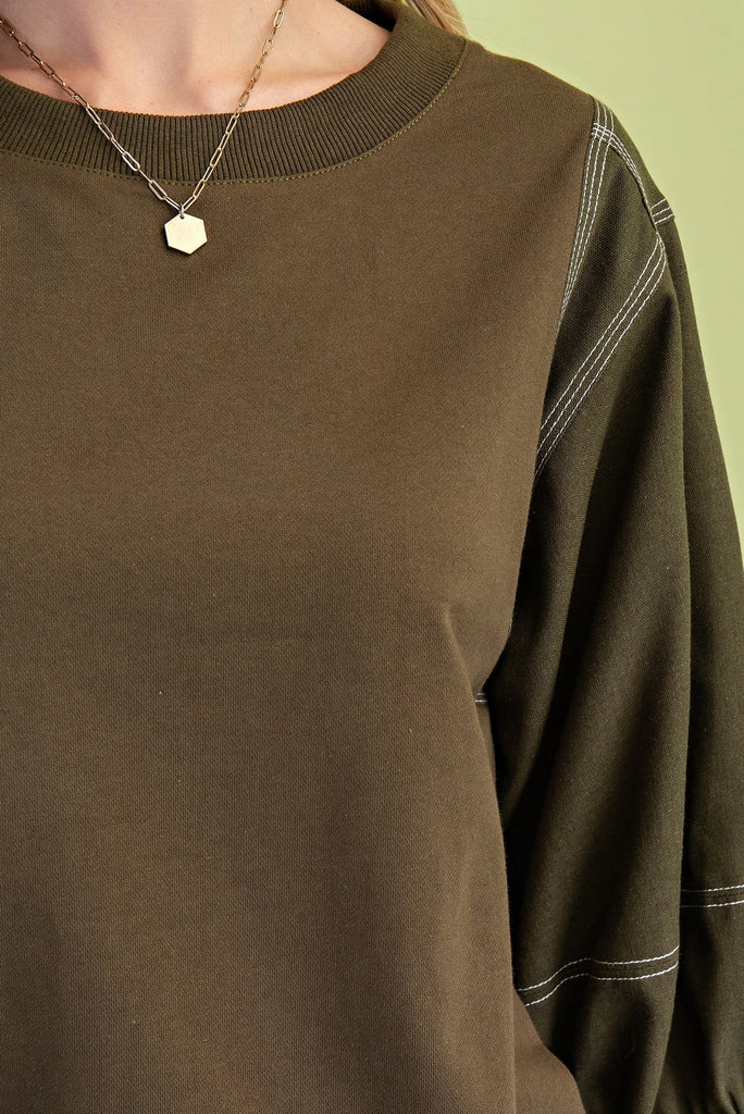 Olive mixed-fabric top with ¾ length sleeves, contrast stitching, crew neckline, and relaxed fit