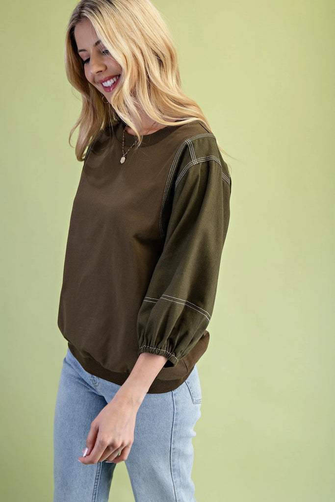 Olive mixed-fabric top with ¾ length sleeves, contrast stitching, crew neckline, and relaxed fit