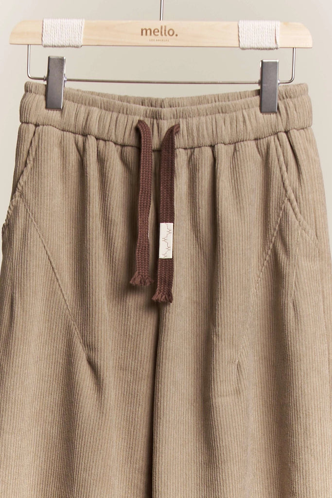 Ottilie Mello corduroy wide-leg crop pants in a neutral beige color, featuring an elastic drawstring waist and a cuffed hem, styled on a hanger.