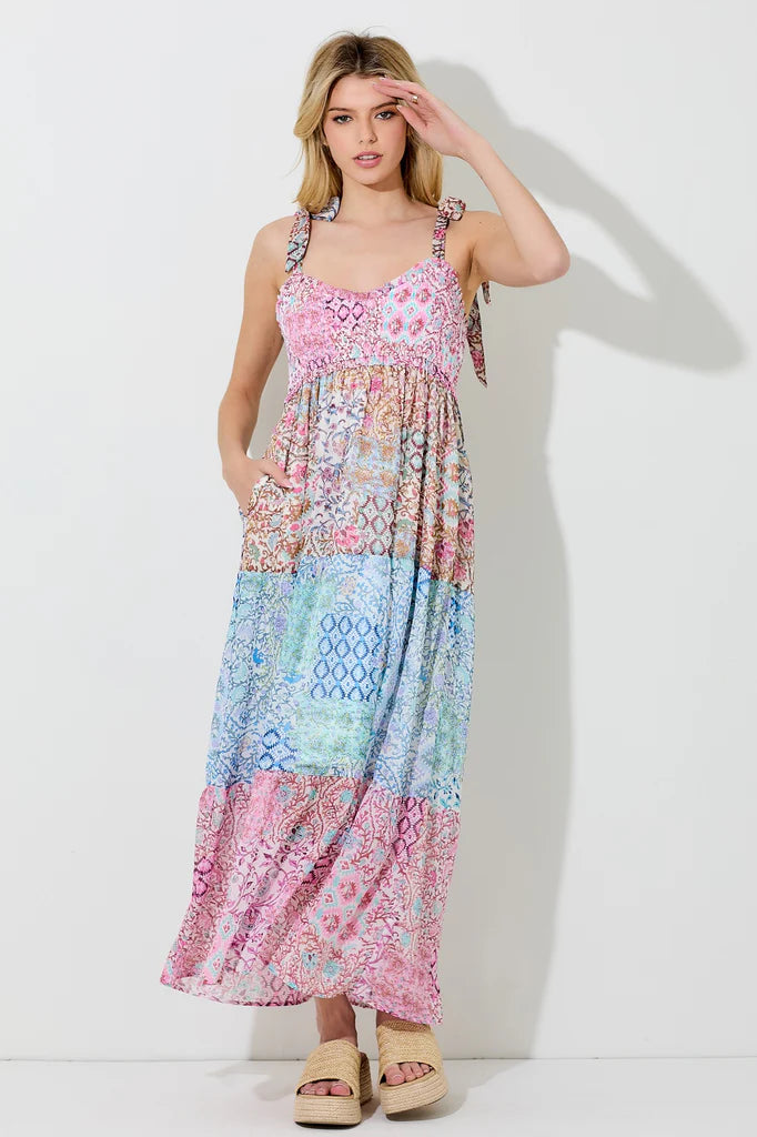 Pink multi floral patchwork-style dress with tie straps, smocked bust, and tiered midi/maxi skirt. Features sleeveless design, side pockets, and a soft, flowy fit.