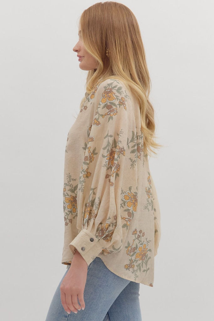 An ecru-colored button-down top with a vintage-style floral print in yellow, green, and orange. The top has a classic collar and long, slightly voluminous sleeves with buttoned cuffs.