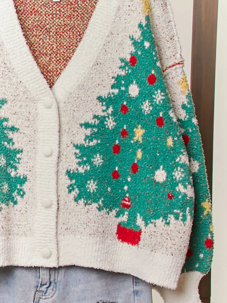 A fuzzy white knit cardigan with a green Christmas tree, red ornament, and yellow star pattern. It has a V-neckline, long sleeves, and a button-up front.