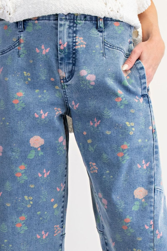 A pair of washed denim barrel-leg pants with a floral print in pink, peach, and green. The pants are high-waisted and cropped at the ankle.