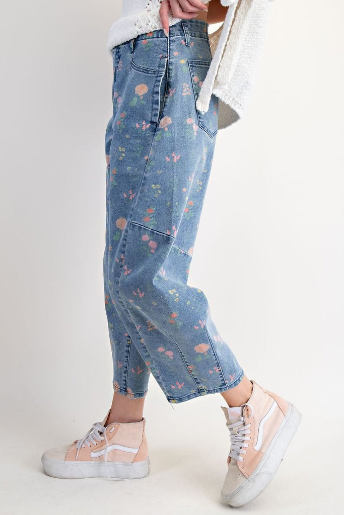 A pair of washed denim barrel-leg pants with a floral print in pink, peach, and green. The pants are high-waisted and cropped at the ankle.