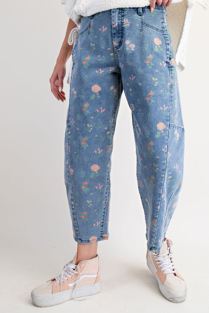 A pair of washed denim barrel-leg pants with a floral print in pink, peach, and green. The pants are high-waisted and cropped at the ankle.