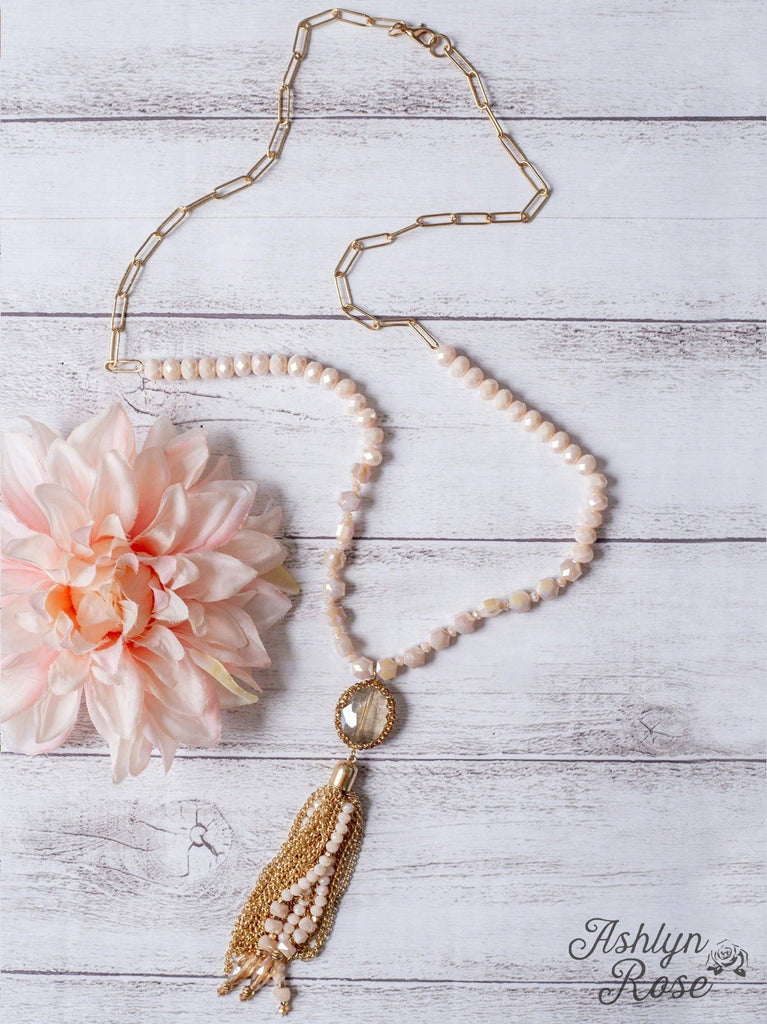 Beaded blush and gold tassel necklace with clear crystal pendant on a gold linked chain.