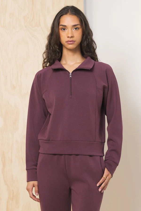 A merlot-colored cloud fleece quarter-zip pullover. It has a collar, long raglan sleeves, and a cropped fit.