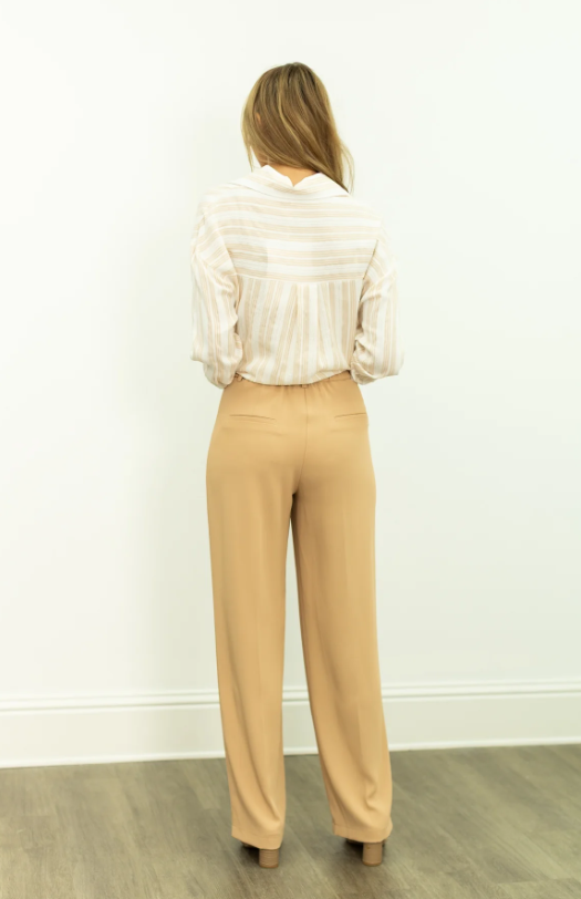 Person wearing a striped shirt and beige pants against a white wall.