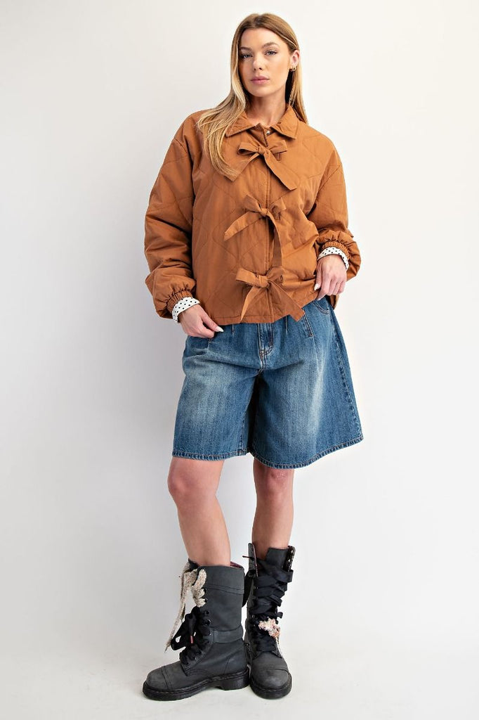 A camel-colored quilted jacket with a three-bow front closure, a collar, and elastic cuffs with a white polka dot pattern.