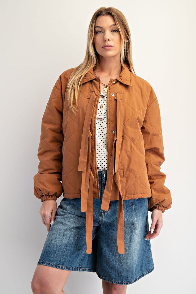 A camel-colored quilted jacket with a three-bow front closure, a collar, and elastic cuffs with a white polka dot pattern.
