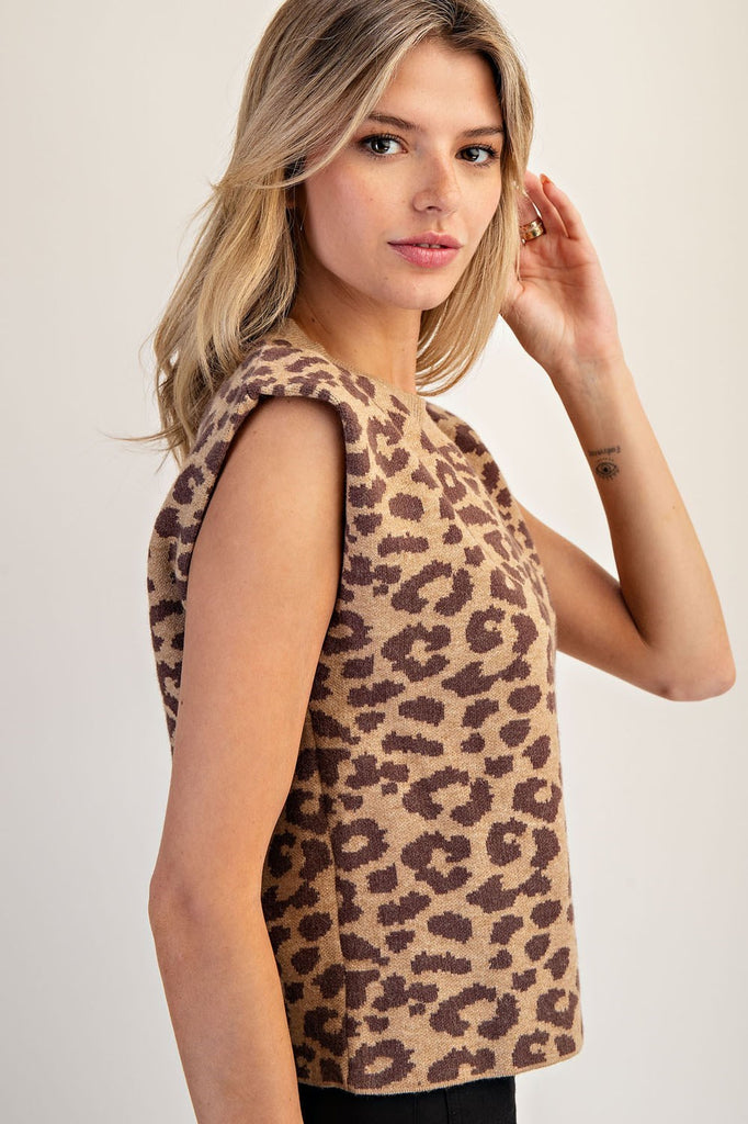 Model wearing a sleeveless leopard print knit sweater with a ribbed crew neckline. The top features a brown and tan allover jacquard animal pattern, lightly padded shoulders for a boxy fit, and is styled with high-waisted black pants.