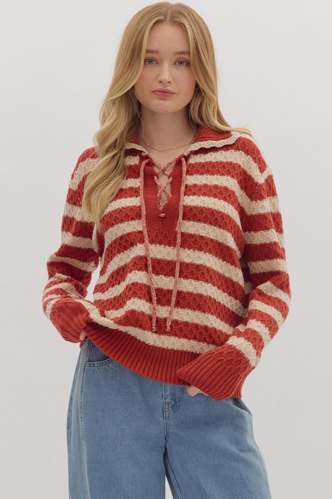 A woman models a striped, long-sleeve sweater in red and cream with a lace-up front and a collar. She is wearing it with light wash jeans.