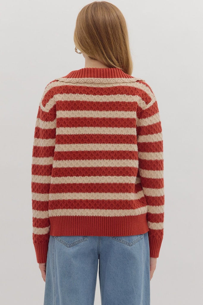 A woman models a striped, long-sleeve sweater in red and cream with a lace-up front and a collar. She is wearing it with light wash jeans.