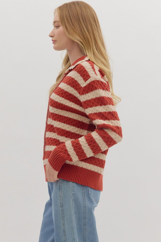 A woman models a striped, long-sleeve sweater in red and cream with a lace-up front and a collar. She is wearing it with light wash jeans.