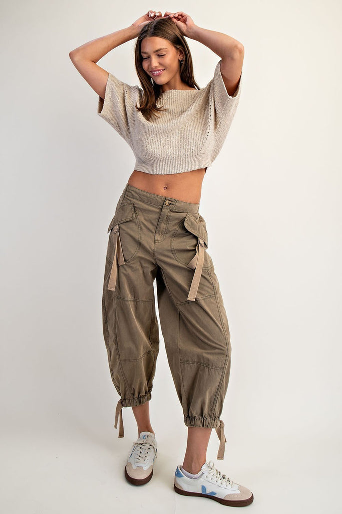 Smiling woman wearing a beige textured knit cropped sweater with half dolman sleeves, a subtle boat neckline, and ribbed hem, paired with olive cargo trousers.