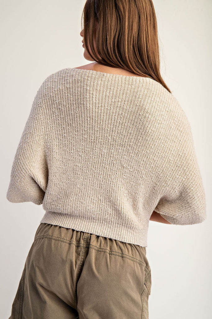 Smiling woman wearing a beige textured knit cropped sweater with half dolman sleeves, a subtle boat neckline, and ribbed hem, paired with olive cargo trousers.