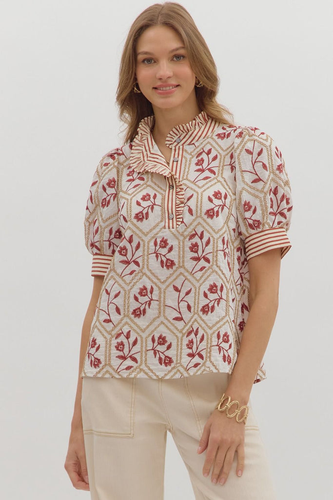 A white top with a brick-red floral and gold chain-link embroidered pattern. It has short puff sleeves, a high ruffled neck, and a front button placket with a contrasting red and white striped pattern.