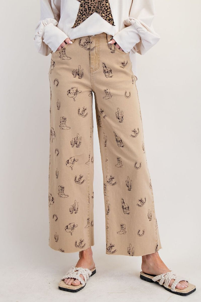 Khaki western printed twill pants with a wide-leg silhouette, button and zip fly, raw hem, and front/back pockets. Features a mixed western pattern on soft, stretchy cotton twill.