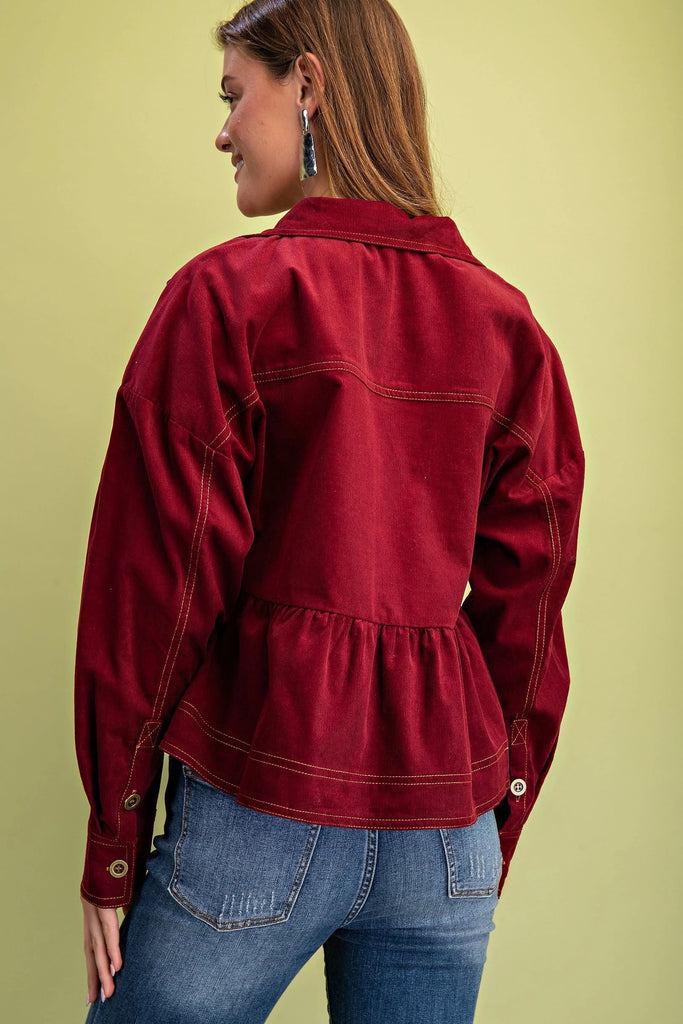 A burgundy corduroy jacket with gold contrast stitching, a button-up front with gold buttons, chest pockets, and a babydoll-style fit.