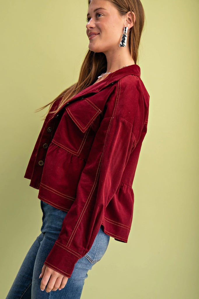 A burgundy corduroy jacket with gold contrast stitching, a button-up front with gold buttons, chest pockets, and a babydoll-style fit.