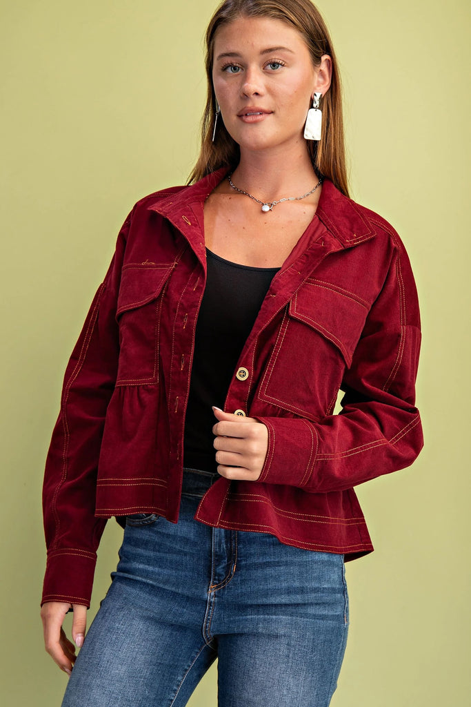 A burgundy corduroy jacket with gold contrast stitching, a button-up front with gold buttons, chest pockets, and a babydoll-style fit.