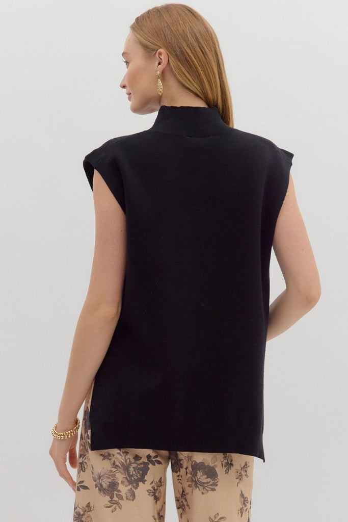 A woman models a solid black, sleeveless, mock-neck sweater with a high-low hem, paired with cute jeans.