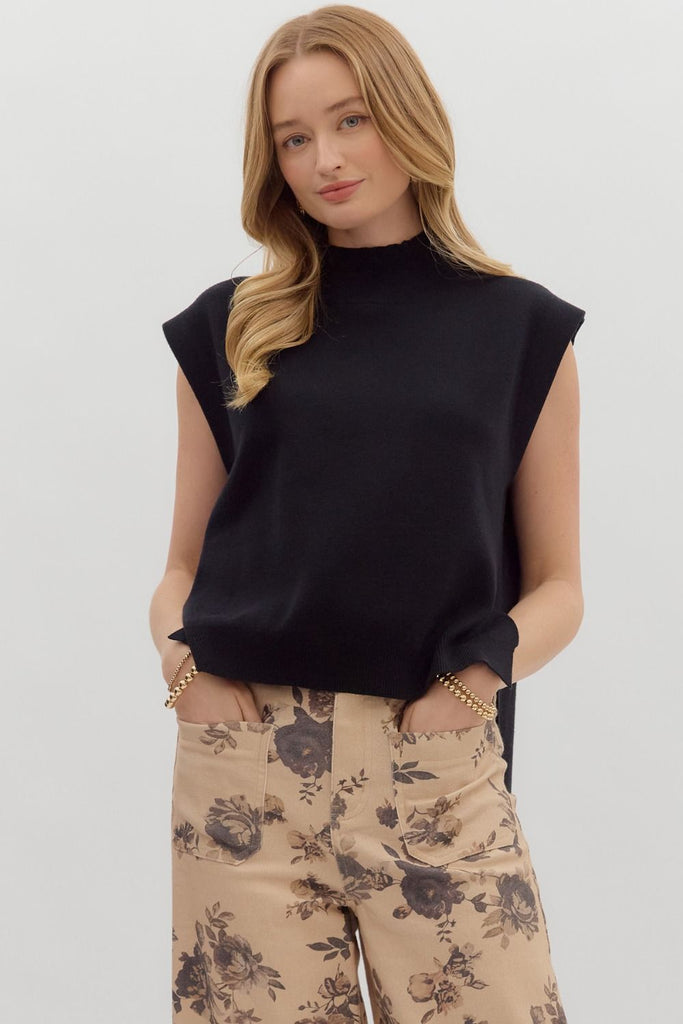 A woman models a solid black, sleeveless, mock-neck sweater with a high-low hem, paired with cute jeans.