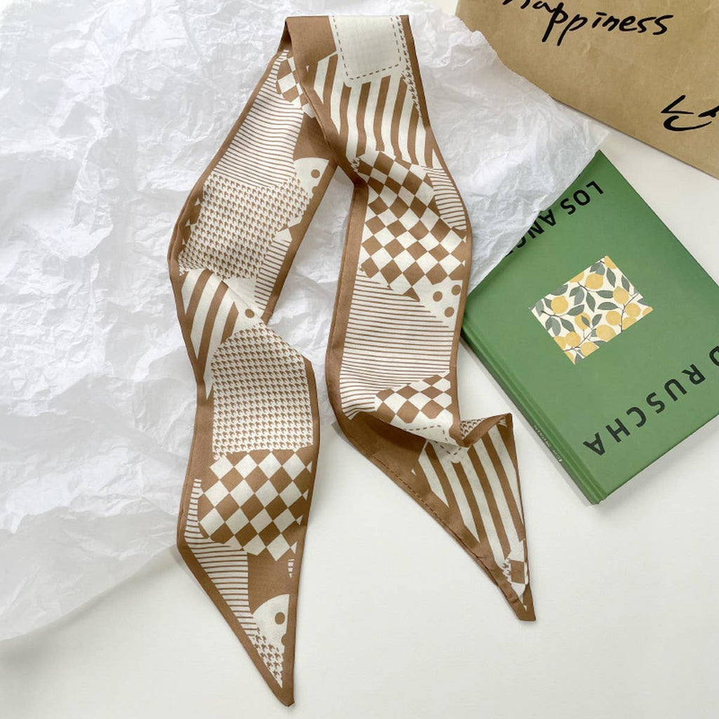 Patterned brown and beige scarf on a textured surface with a green book and brown paper bag.