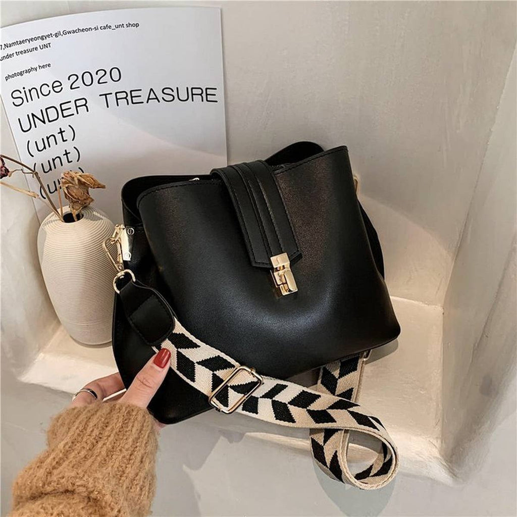 Black handbag with a patterned strap held by a hand against a light background