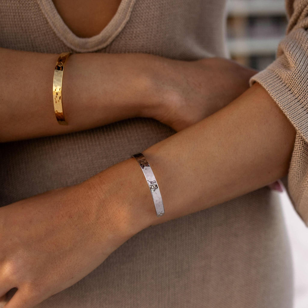 Two wrists wearing gold and silver bracelets against a neutral background