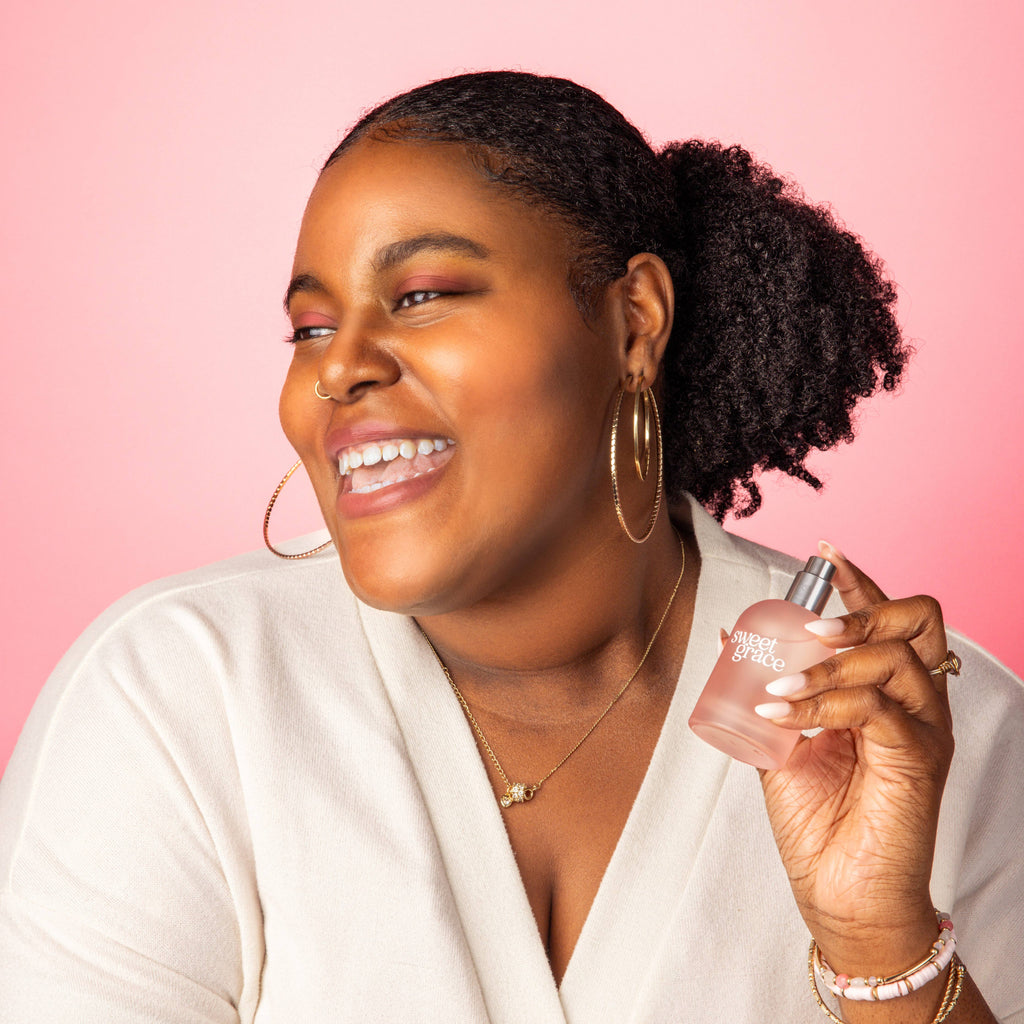 Woman holding a perfume bottle against a pink background
