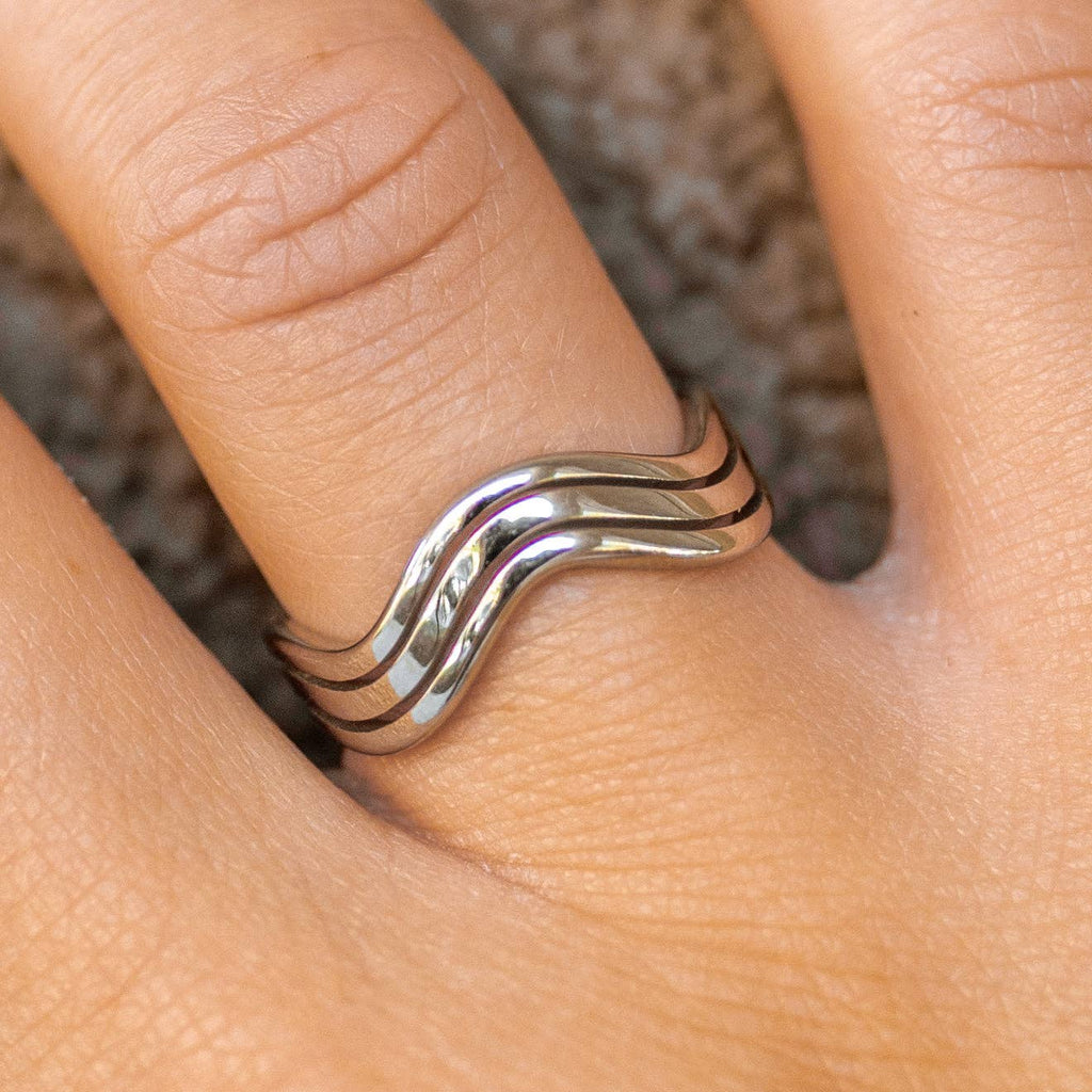Silver wavy ring on a finger with a neutral background