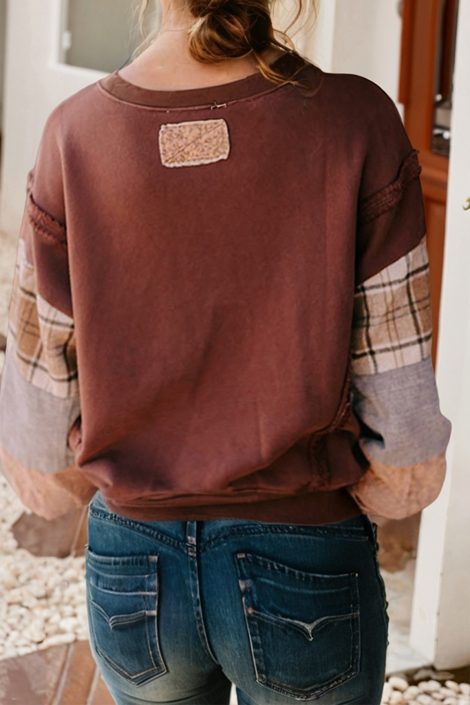Person wearing a brown sweatshirt with plaid sleeves and blue jeans, standing outdoors.